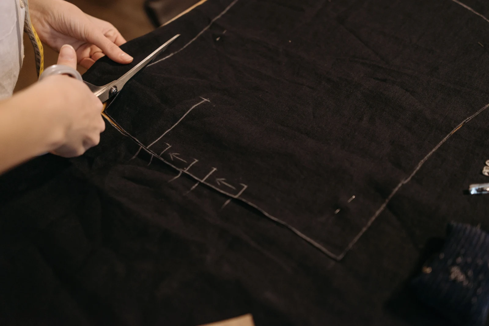 Hands cutting black fabric along marked pattern lines — representative stock photograph